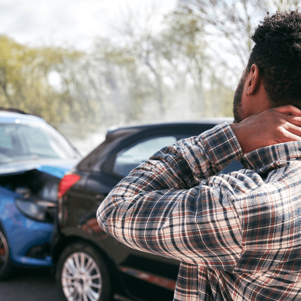 Homme de dos se tenant la nuque avec en arrière plan une collision entre deux voitures lors d'un accident de la route
