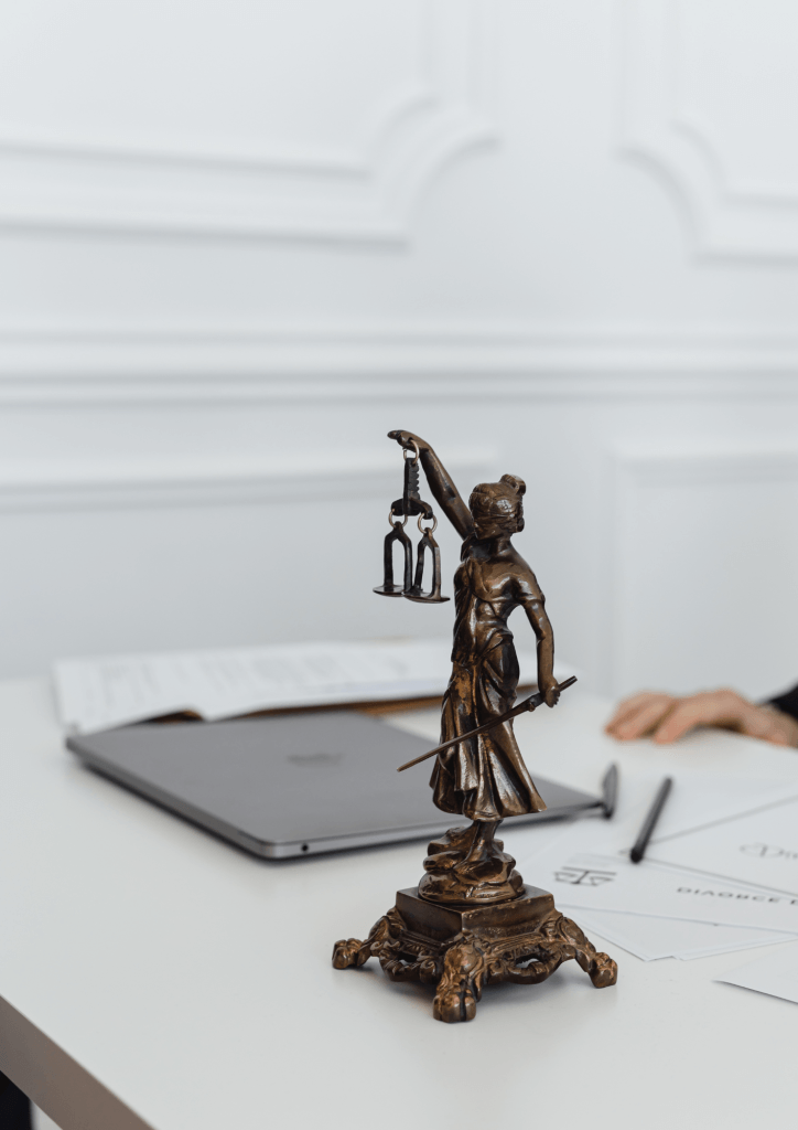 Photo d'une statuette en bronze de Thémis, déesse de la justice, posée sur un bureau à côté d'un ordinateur portable